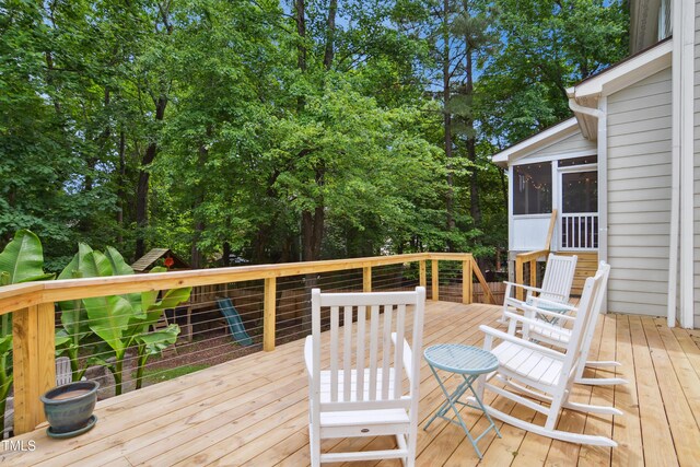 wooden terrace with a sunroom and view of wooded area