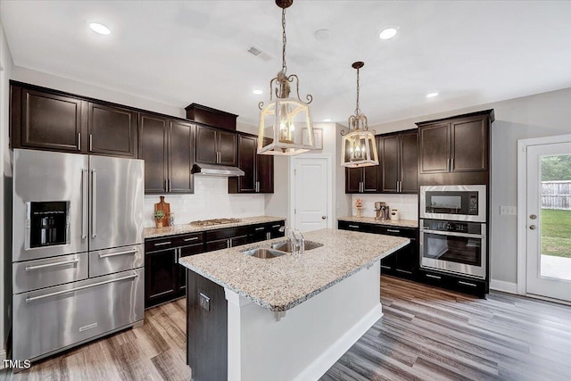 kitchen with stainless steel appliances, a sink, dark brown cabinets, wood finished floors, and recessed lighting