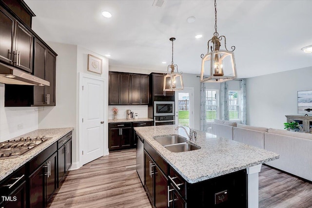 kitchen with a sink, appliances with stainless steel finishes, light wood-style floors, open floor plan, and under cabinet range hood