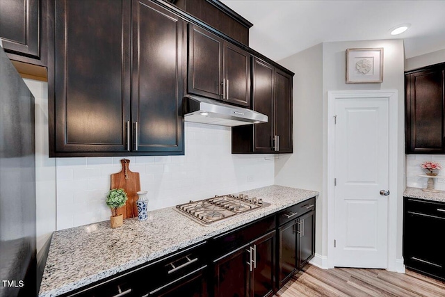 kitchen with under cabinet range hood, stainless steel gas stovetop, tasteful backsplash, light wood-style flooring, and light stone counters