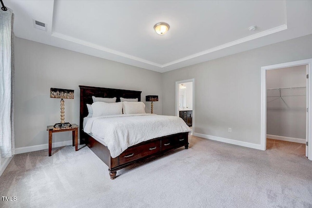 bedroom featuring a raised ceiling, light colored carpet, baseboards, a walk in closet, and ensuite bathroom