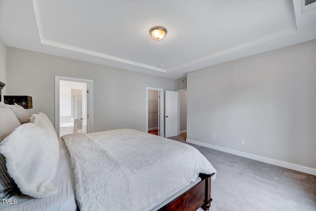 bedroom featuring a raised ceiling, baseboards, carpet floors, ensuite bath, and a walk in closet