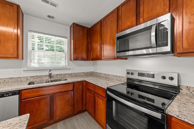 204 Trevor Ridge Dr, Holly Springs, NC 27540 - kitchen featuring appliances with stainless steel finishes, brown cabinetry, light wood-style flooring, and light stone counters
