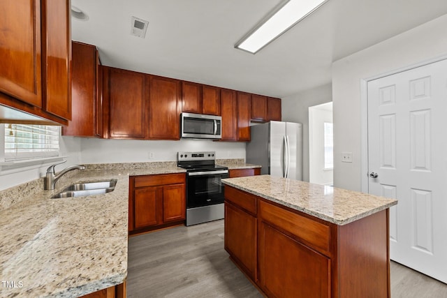 204 Trevor Ridge Dr, Holly Springs, NC 27540 - kitchen featuring appliances with stainless steel finishes, light wood-type flooring, a center island, light stone countertops, and brown cabinets