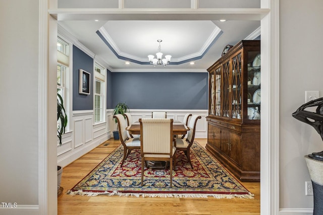 dining space with wood finished floors, a chandelier, ornamental molding, a tray ceiling, and a wainscoted wall