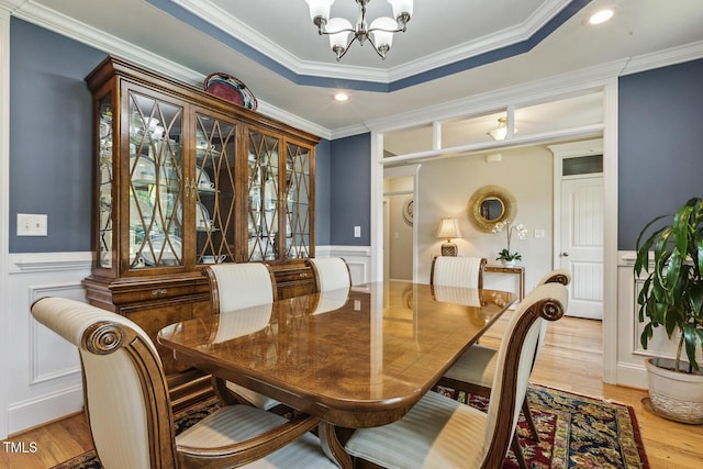 dining area with a chandelier, light wood finished floors, a wainscoted wall, a decorative wall, and ornamental molding