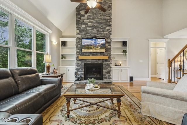 living area with high vaulted ceiling, ceiling fan, a stone fireplace, wood finished floors, and stairway