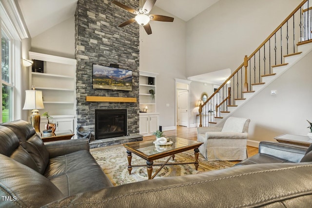 living room with high vaulted ceiling, stairs, ceiling fan, a fireplace, and wood finished floors