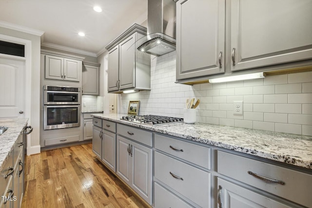 kitchen with gray cabinetry, wall chimney range hood, appliances with stainless steel finishes, crown molding, and tasteful backsplash