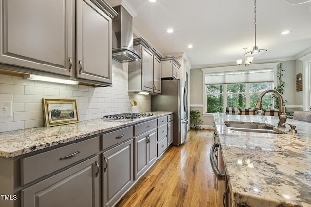 kitchen featuring gray cabinets, a sink, wall chimney range hood, appliances with stainless steel finishes, and ornamental molding