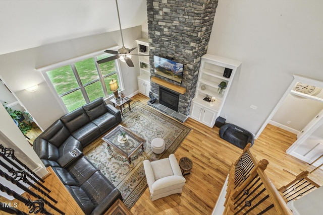 living area featuring wood finished floors, a ceiling fan, a stone fireplace, a high ceiling, and baseboards