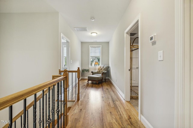 hall featuring light wood-style floors, an upstairs landing, and baseboards