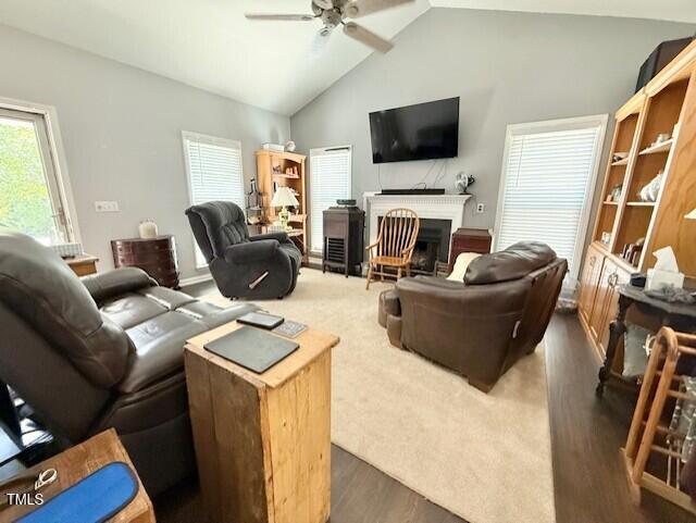 living area featuring vaulted ceiling, ceiling fan, a fireplace, and dark wood-type flooring