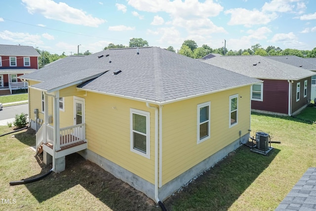 rear view of property with cooling unit, a lawn, and a shingled roof