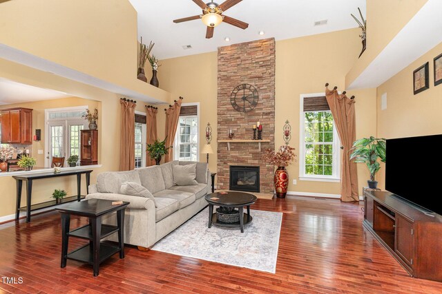 living area with a high ceiling, a ceiling fan, wood finished floors, a stone fireplace, and baseboards