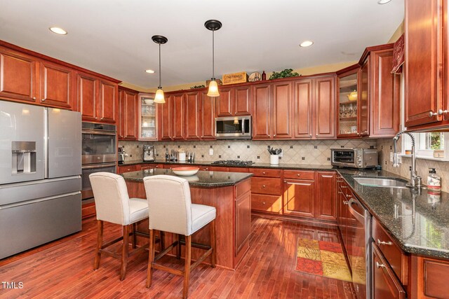 kitchen with stainless steel appliances, a sink, dark wood-type flooring, a center island, and glass insert cabinets