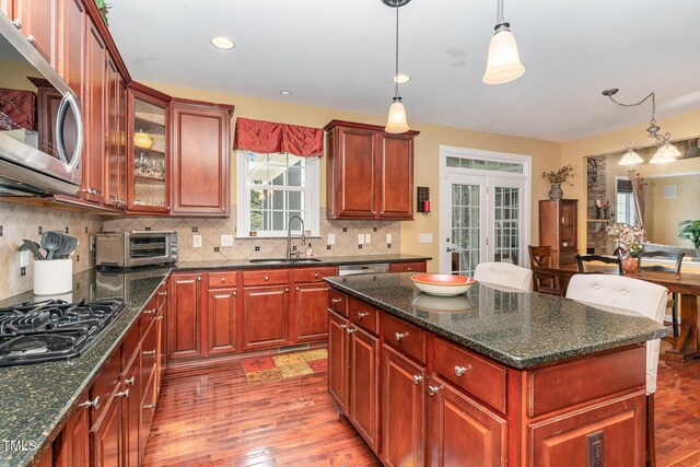 kitchen with a sink, stainless steel microwave, black gas cooktop, decorative backsplash, and pendant lighting