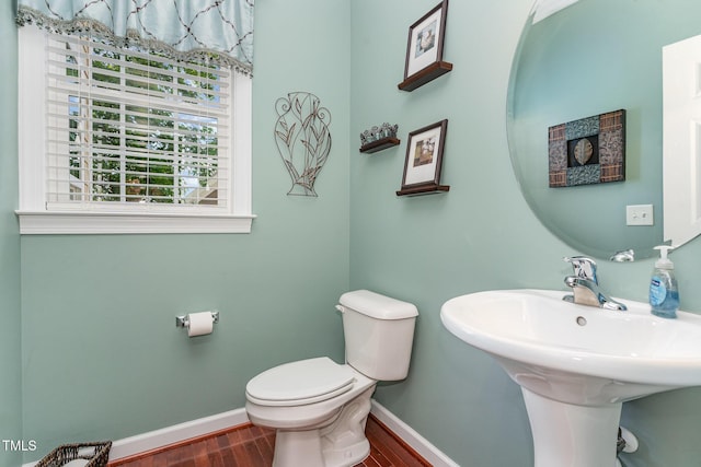 half bath with baseboards, wood finished floors, toilet, and a sink