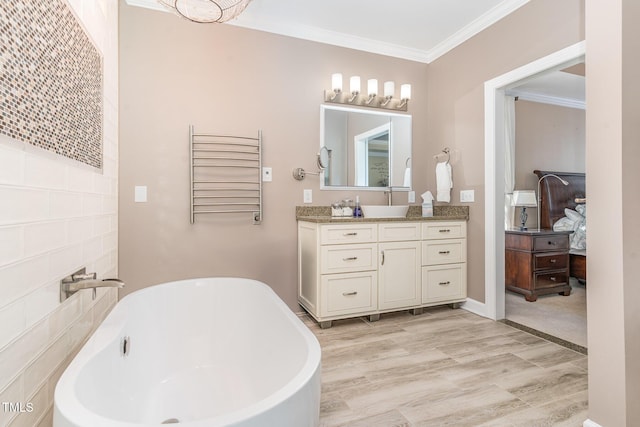 ensuite bathroom with ornamental molding, a freestanding tub, vanity, and wood finished floors