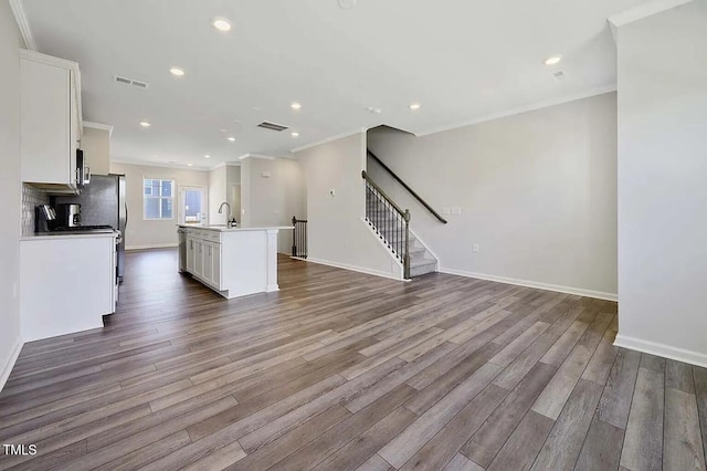 kitchen with white cabinets, ornamental molding, dark wood finished floors, open floor plan, and a kitchen island with sink