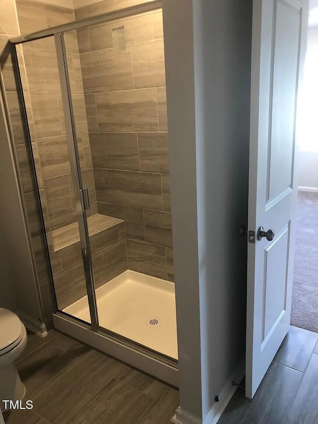 bathroom with a stall shower, toilet, wood finished floors, and baseboards