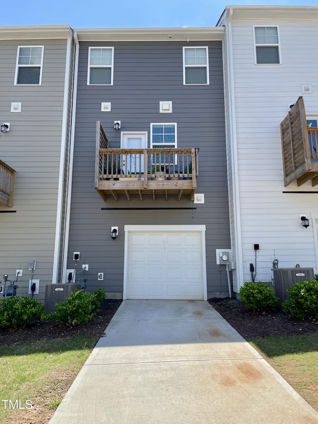 rear view of house with an attached garage, concrete driveway, central AC unit, and a balcony