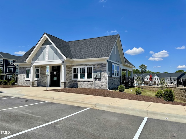 view of front of home featuring board and batten siding, stone siding, uncovered parking, and roof with shingles