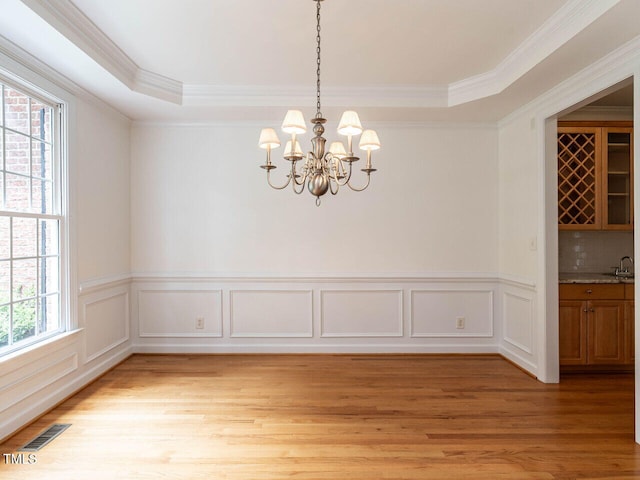 203 Chilcott Ln, Apex, NC 27502 - unfurnished dining area featuring crown molding, light wood-style floors, a chandelier, a tray ceiling, and wainscoting