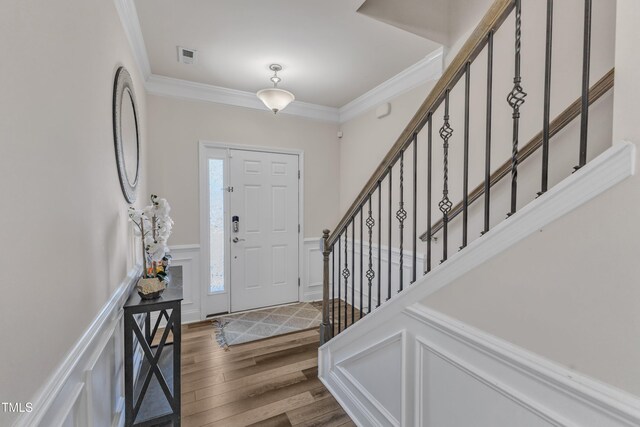 entryway featuring wood finished floors, ornamental molding, a decorative wall, a wainscoted wall, and stairway
