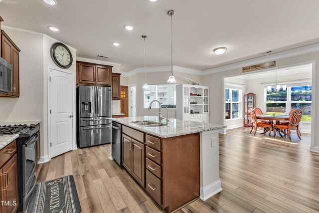kitchen with stainless steel appliances, a sink, ornamental molding, light wood finished floors, and light stone counters