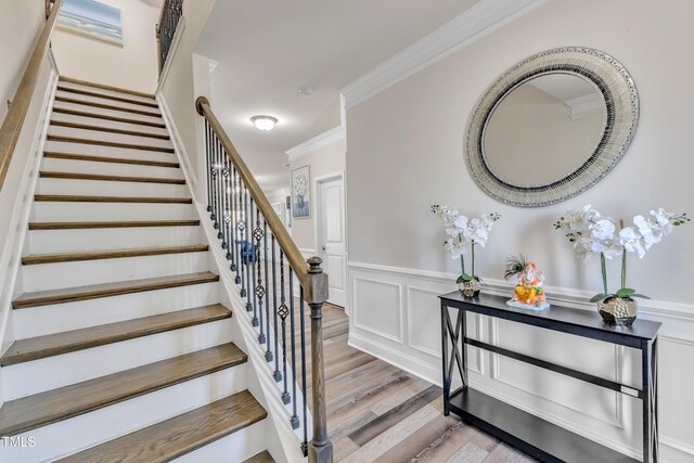 stairs featuring wood finished floors, crown molding, a wainscoted wall, and a decorative wall