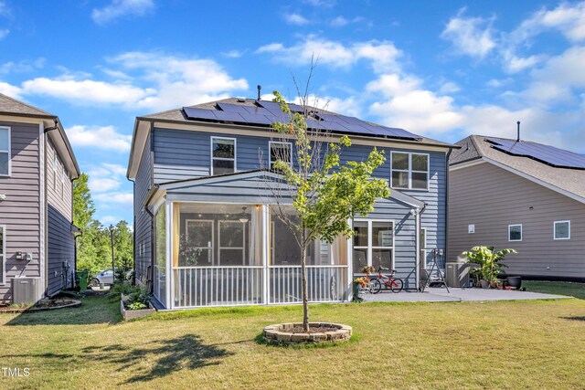 back of house featuring a patio, a sunroom, roof mounted solar panels, and a lawn