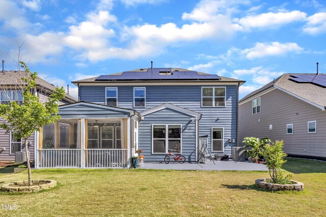 rear view of house with a sunroom, a patio, a lawn, and solar panels