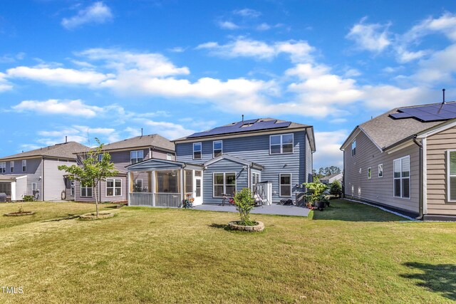 rear view of property featuring a patio area, a yard, a sunroom, and solar panels