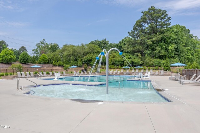 community pool with fence, a patio, and view of wooded area