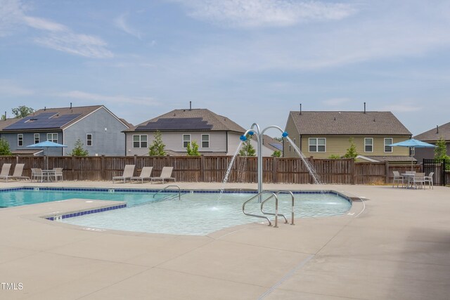 community pool with a residential view, fence, a patio area, and a water slide