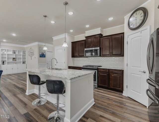 kitchen featuring appliances with stainless steel finishes, a sink, crown molding, wood finished floors, and tasteful backsplash
