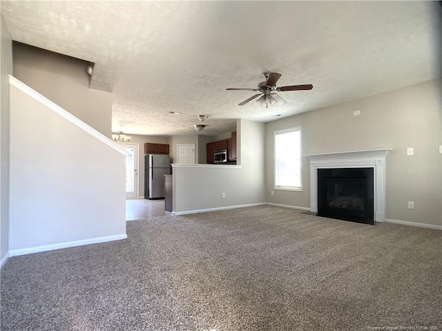unfurnished living room with light colored carpet, baseboards, a fireplace with flush hearth, a ceiling fan, and a textured ceiling