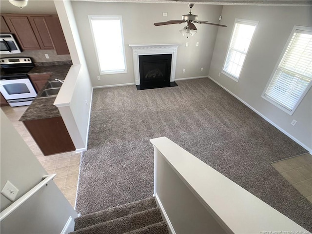 unfurnished living room featuring light carpet, a ceiling fan, baseboards, and a fireplace with flush hearth