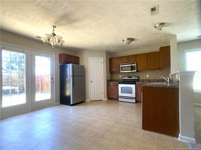 kitchen featuring stainless steel appliances, dark countertops, a sink, a chandelier, and brown cabinetry