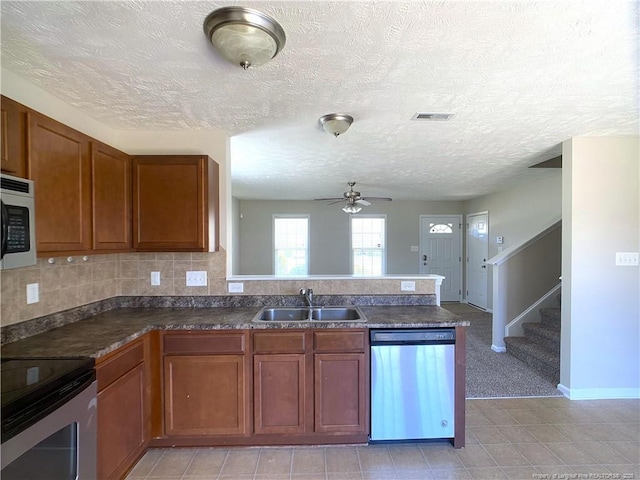 kitchen featuring stainless steel appliances, a sink, brown cabinets, a peninsula, and a ceiling fan