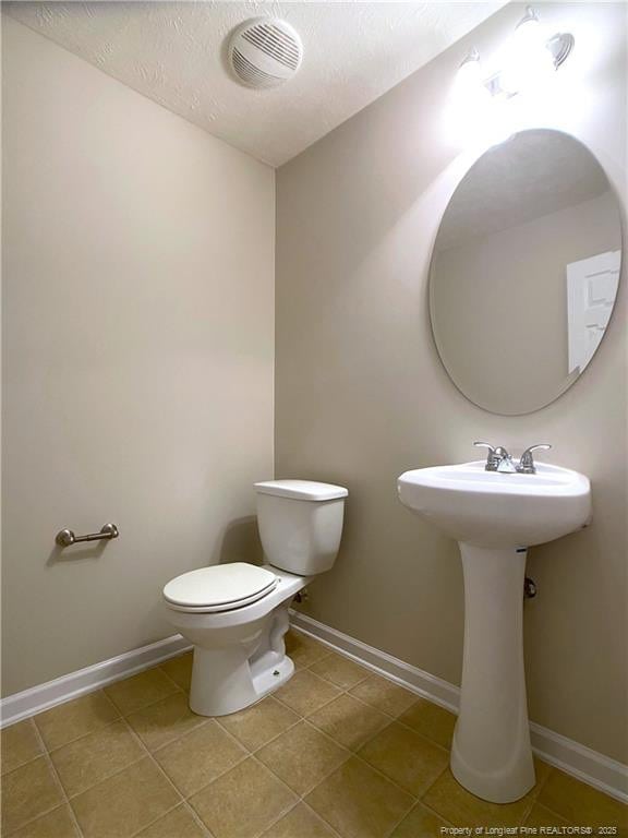 half bath featuring toilet, tile patterned flooring, baseboards, and a textured ceiling