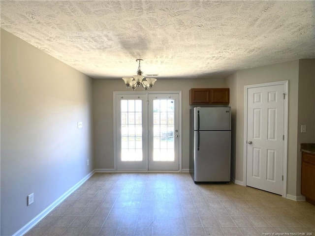 unfurnished dining area with a chandelier, a textured ceiling, and baseboards