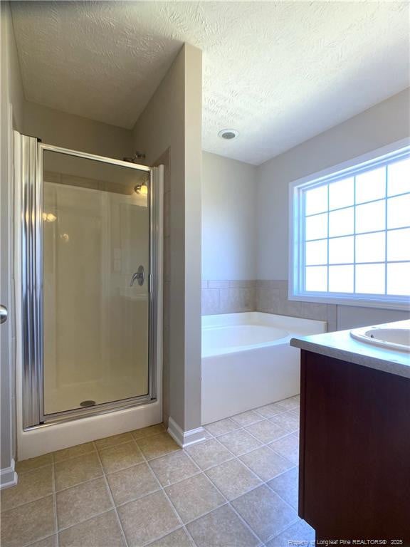 full bath featuring a textured ceiling, tile patterned flooring, a stall shower, a garden tub, and vanity
