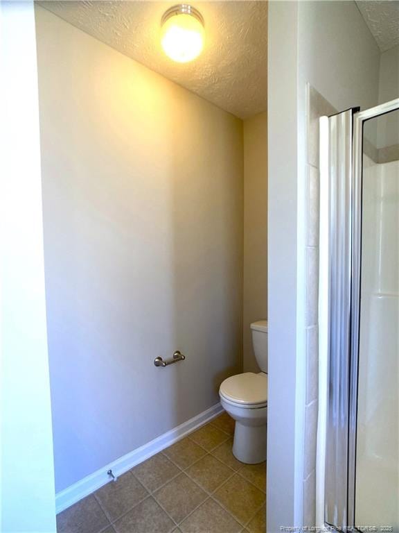bathroom with a textured ceiling, a stall shower, toilet, tile patterned flooring, and baseboards