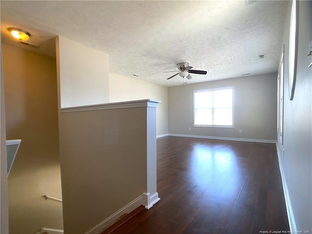 empty room with a textured ceiling, baseboards, a ceiling fan, and dark wood-style flooring