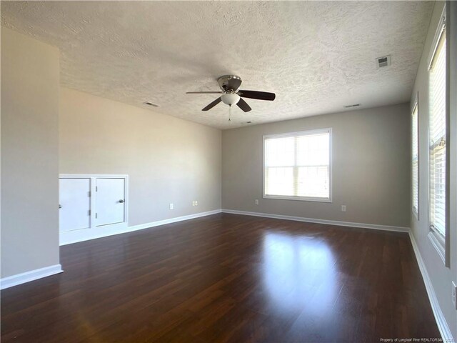 empty room featuring a textured ceiling, ceiling fan, dark wood-type flooring, and baseboards
