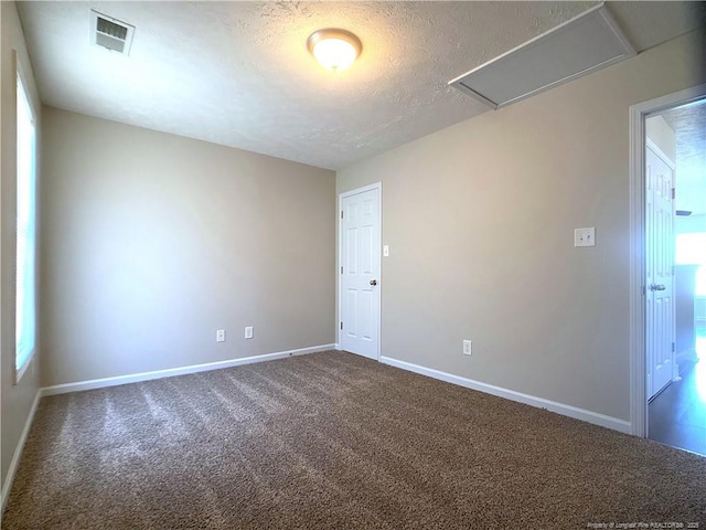 unfurnished room with dark colored carpet, attic access, baseboards, a textured ceiling, and healthy amount of natural light