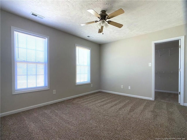empty room with a textured ceiling, carpet floors, baseboards, and a ceiling fan