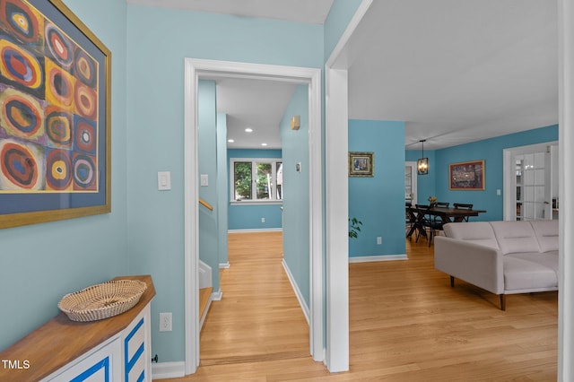 corridor featuring light wood-style floors, baseboards, recessed lighting, and stairs